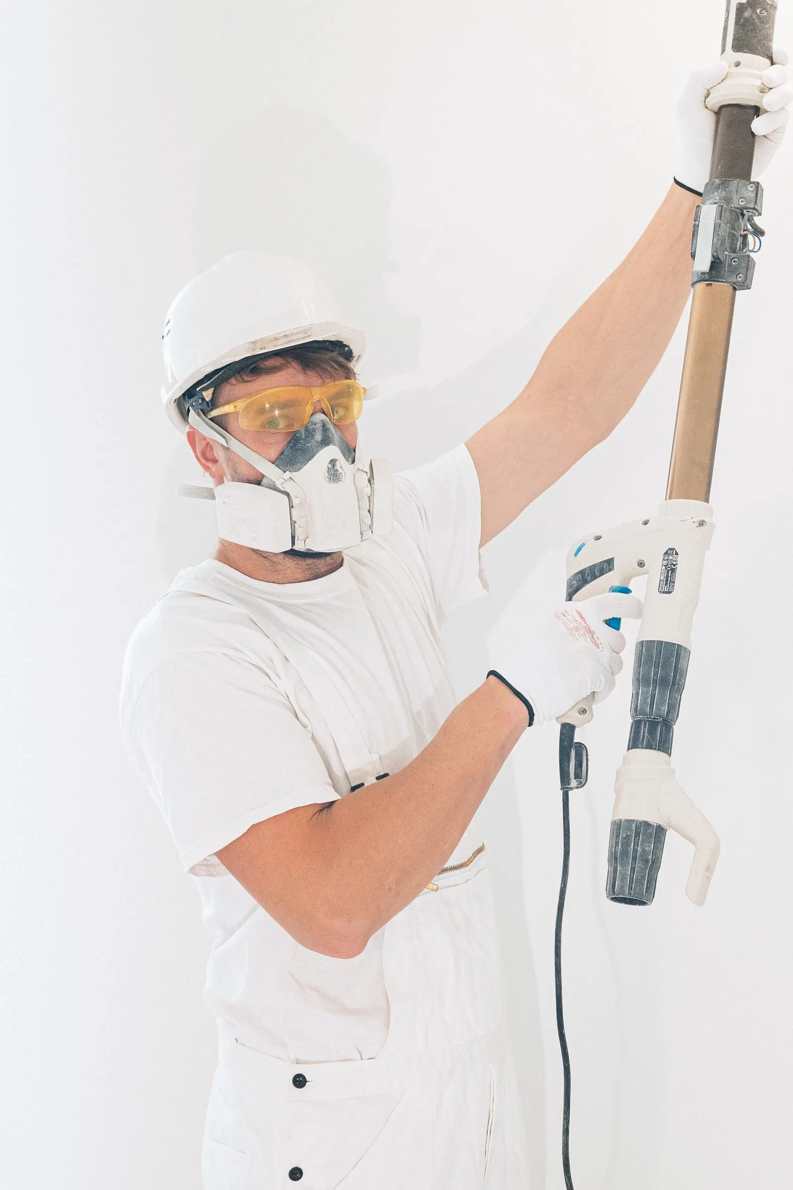 Handyman in protective gear using a power tool on an interior wall