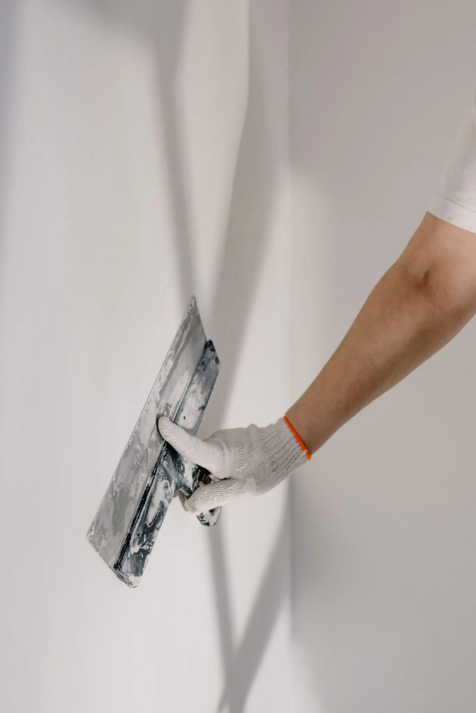 Gloved hand plastering a wall with a trowel