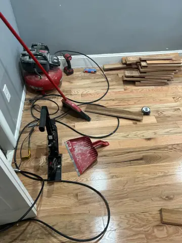 Hardwood flooring installation in progress with a nail gun and compressor