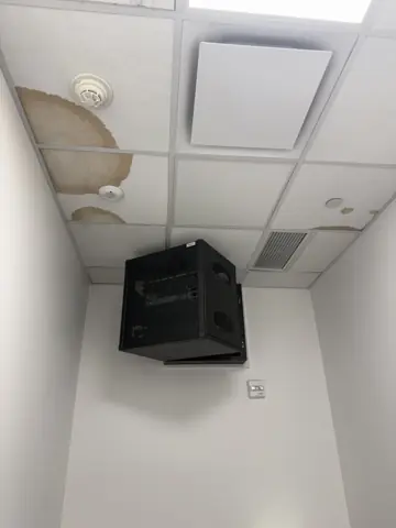 Office ceiling with water-damaged tiles near a mounted TV