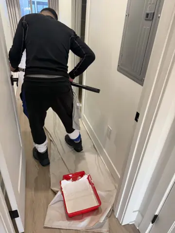 Painting walls with a roller in a hallway with drop cloths down